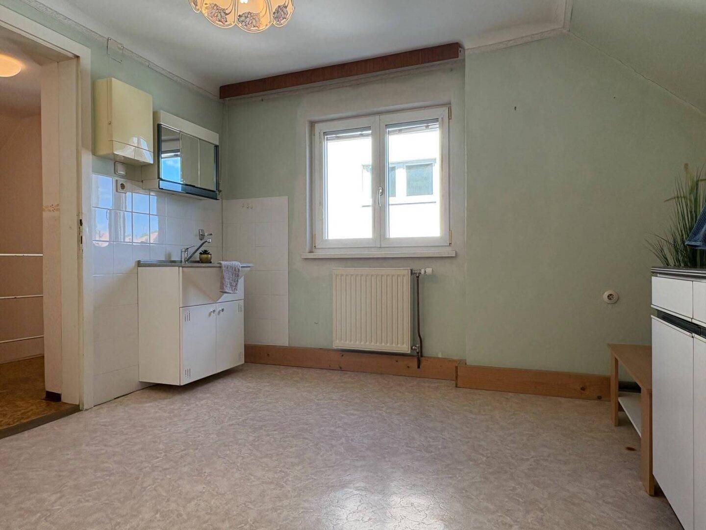 Dachgeschosszimmer mit kleiner Küchenzeile, Fenster und Schräge, praktisch eingerichtet.