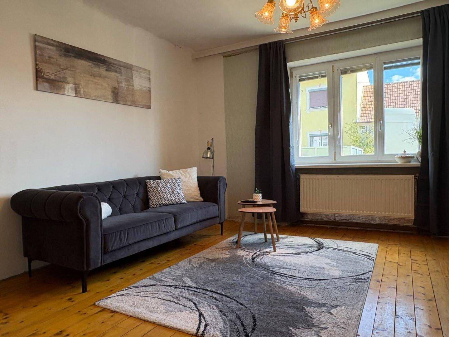 Helles Wohnzimmer mit bequemer Couch, Holzdielen und Blick nach draußen, modern eingerichtet.