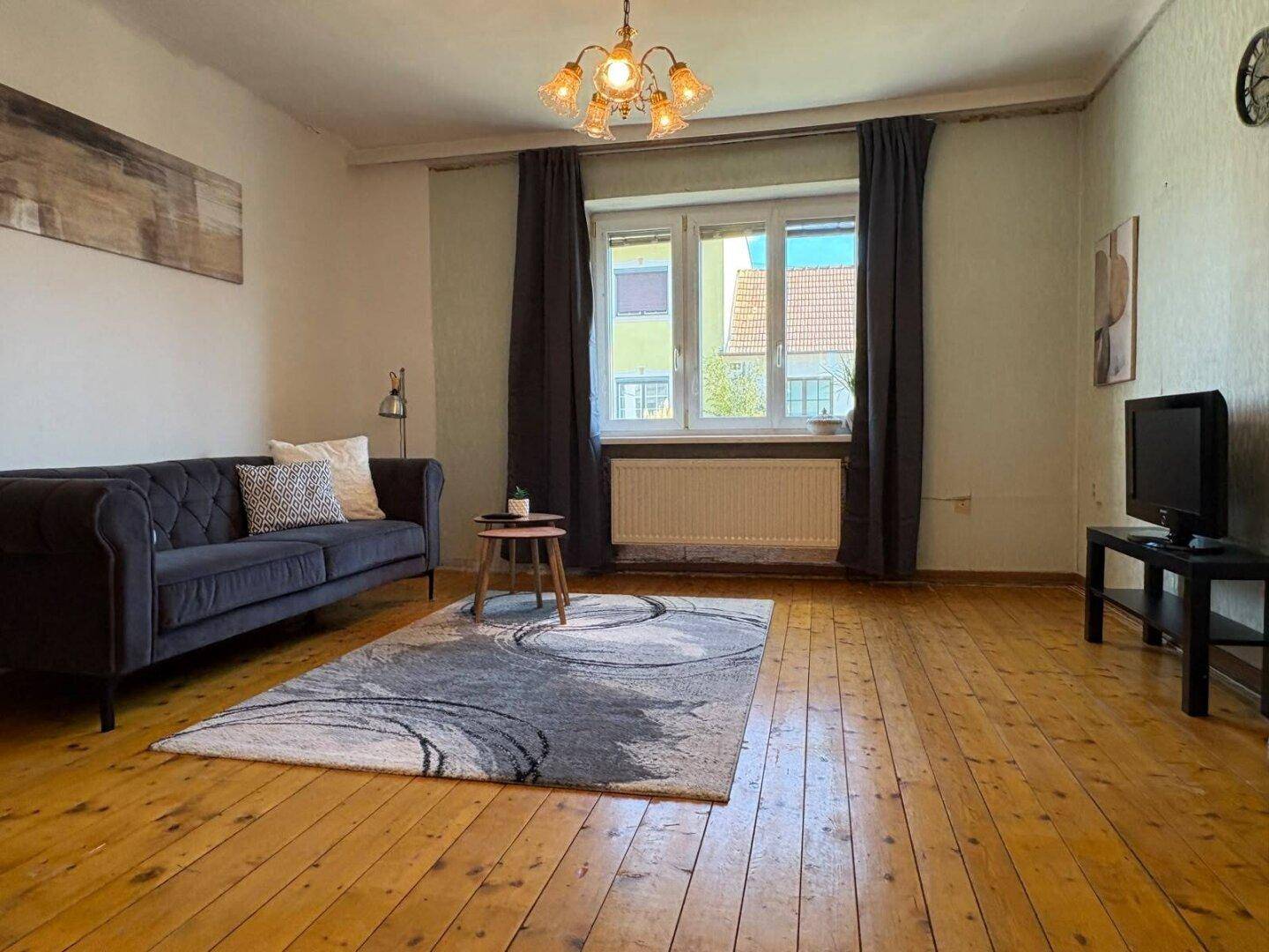 Gemütliches Wohnzimmer mit Holzdielenboden, Sofa und großem Fenster, hell und einladend.