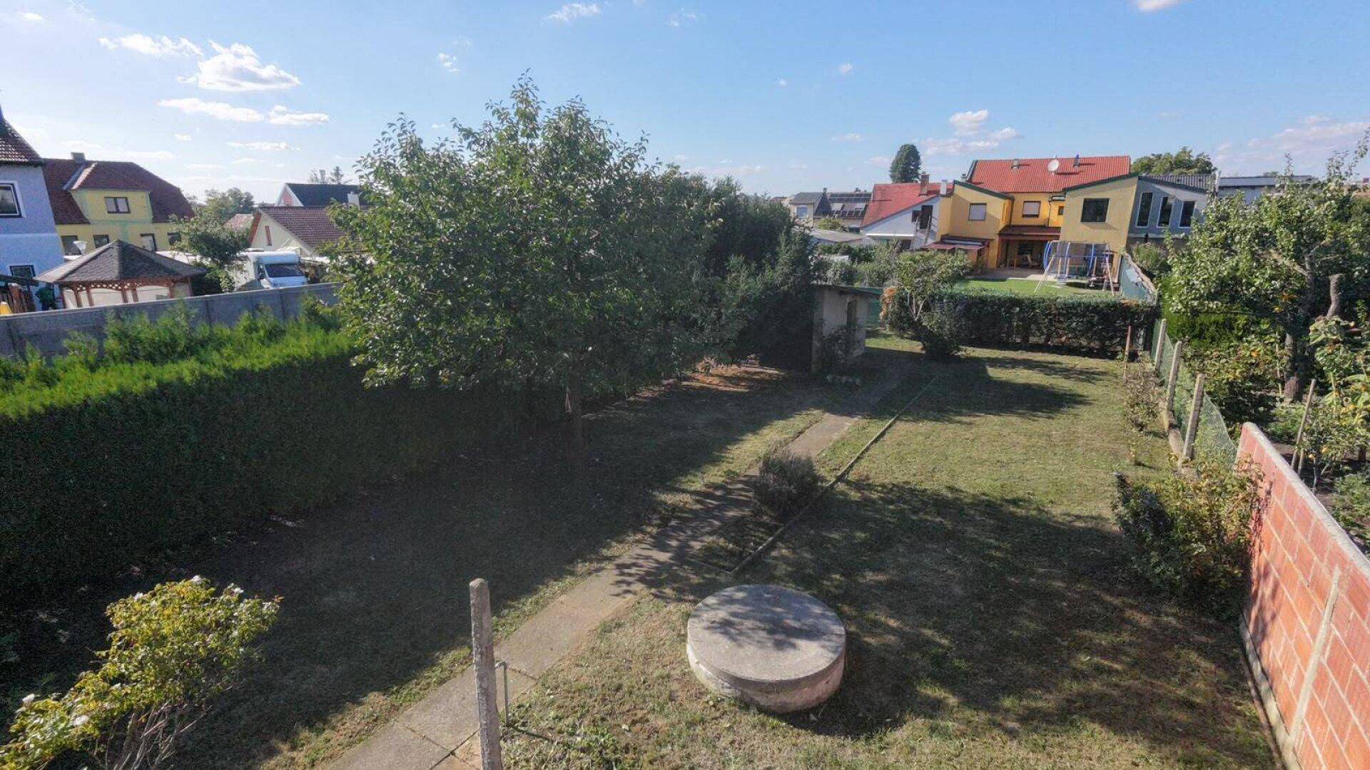 Gartenansicht von oben mit Rasen, Bäumen und umliegenden Häusern, weitläufig und grün.