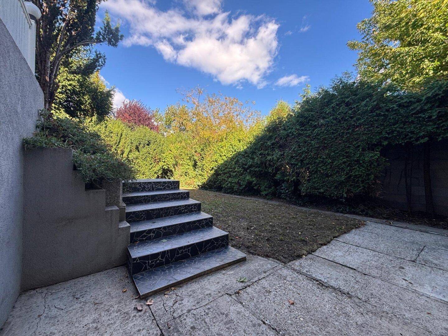 Gepflegter Gartenbereich mit Steintreppe und Rasenfläche, umgeben von Grün.