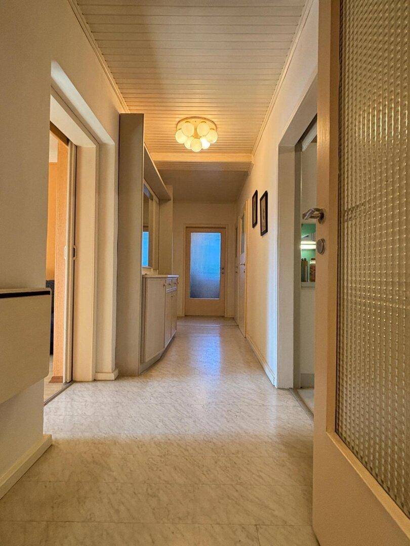 Heller Flur mit Holzdeckenverkleidung und Marmorboden, der zu weiteren Räumen führt.