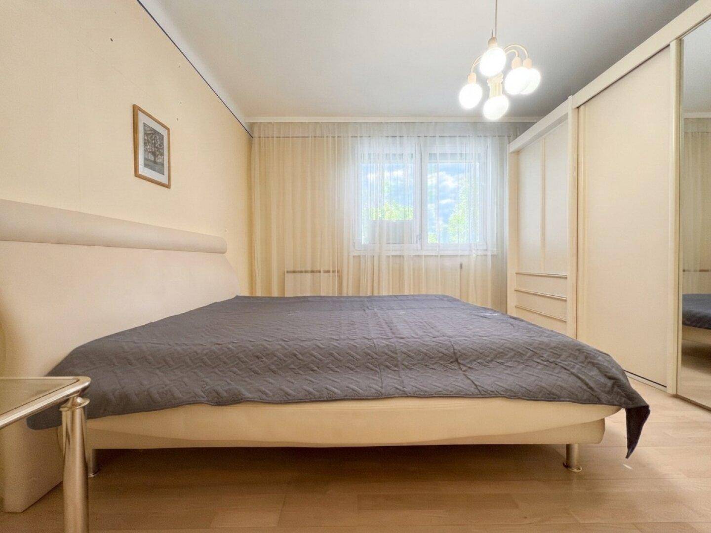 Helles Schlafzimmer mit großem Fenster, Holzboden und geräumigem Kleiderschrank.