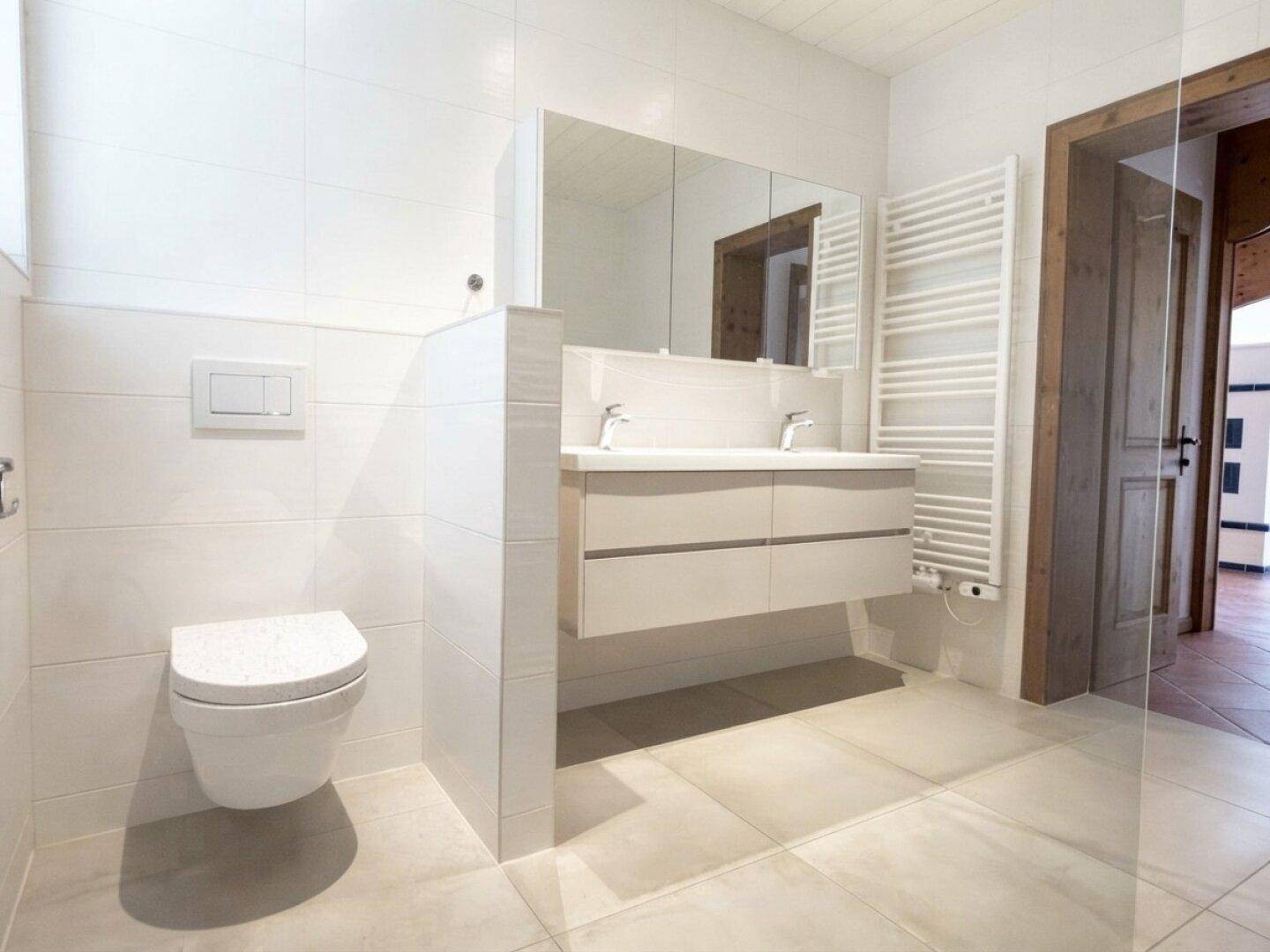 Helles Badezimmer mit Doppelwaschtisch, Wand-WC und beheiztem Handtuchhalter.