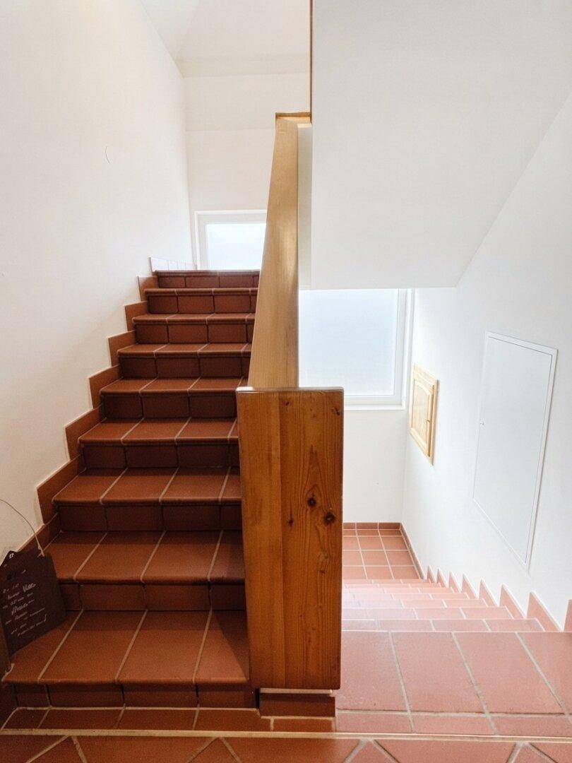 Treppenhaus mit Terrakottafliesen und Holzgeländer, das die verschiedenen Etagen verbindet.