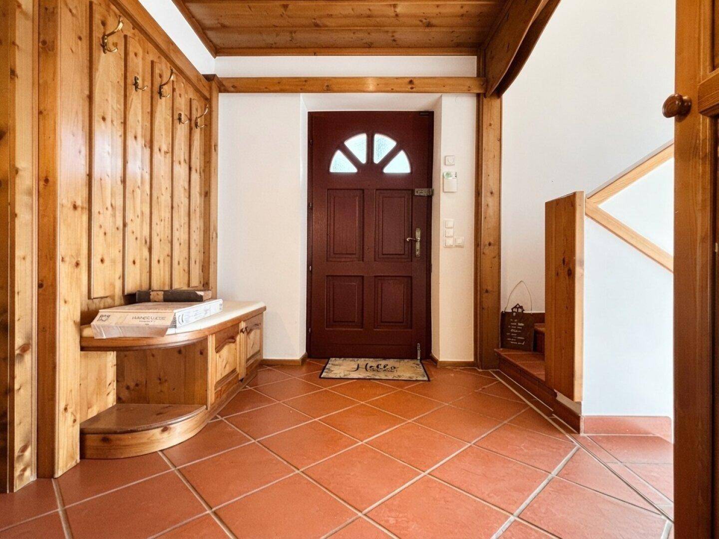 Eingangsbereich mit Holztäfelung, Garderobe und Terrakottafliesen, führt zu einer Holztreppe.