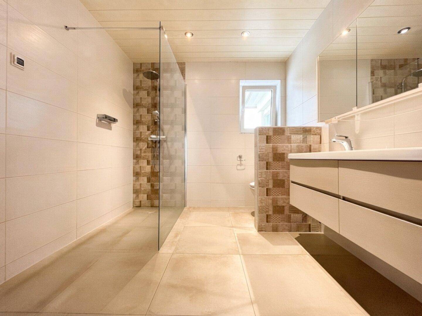 Geräumiges Badezimmer mit begehbarer Dusche, Doppelwaschtisch und Fenster für natürliche Belüftung.
