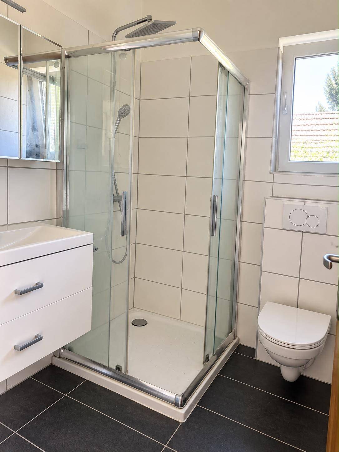 Modernes Badezimmer mit Duschkabine, wandhängendem WC und Fenster.