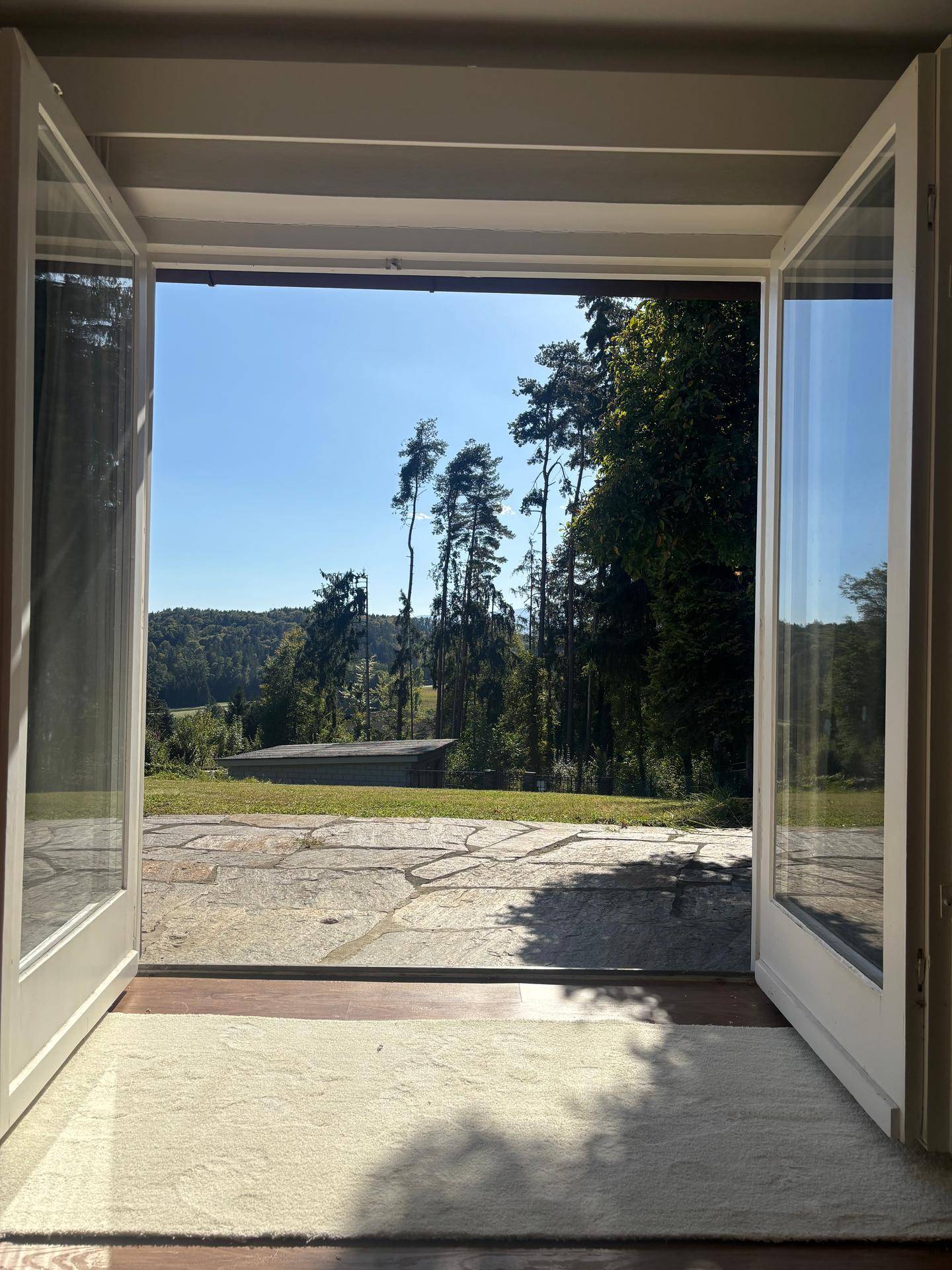 Offene Terrassentüren bieten einen weiten Blick auf die grüne Landschaft und den Garten.