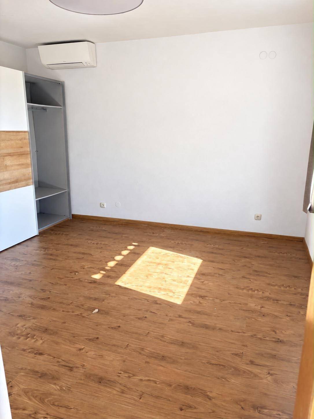Helles Schlafzimmer mit Laminatboden, Einbauschrank und Klimaanlage.