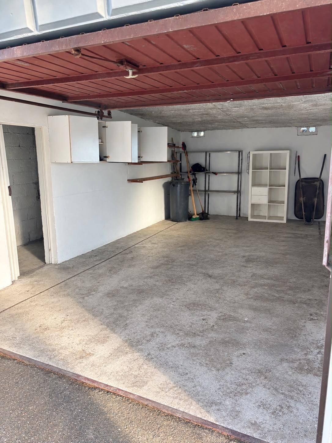 Innenansicht der Garage mit Betonboden, Regalen und Schränken für Stauraum.