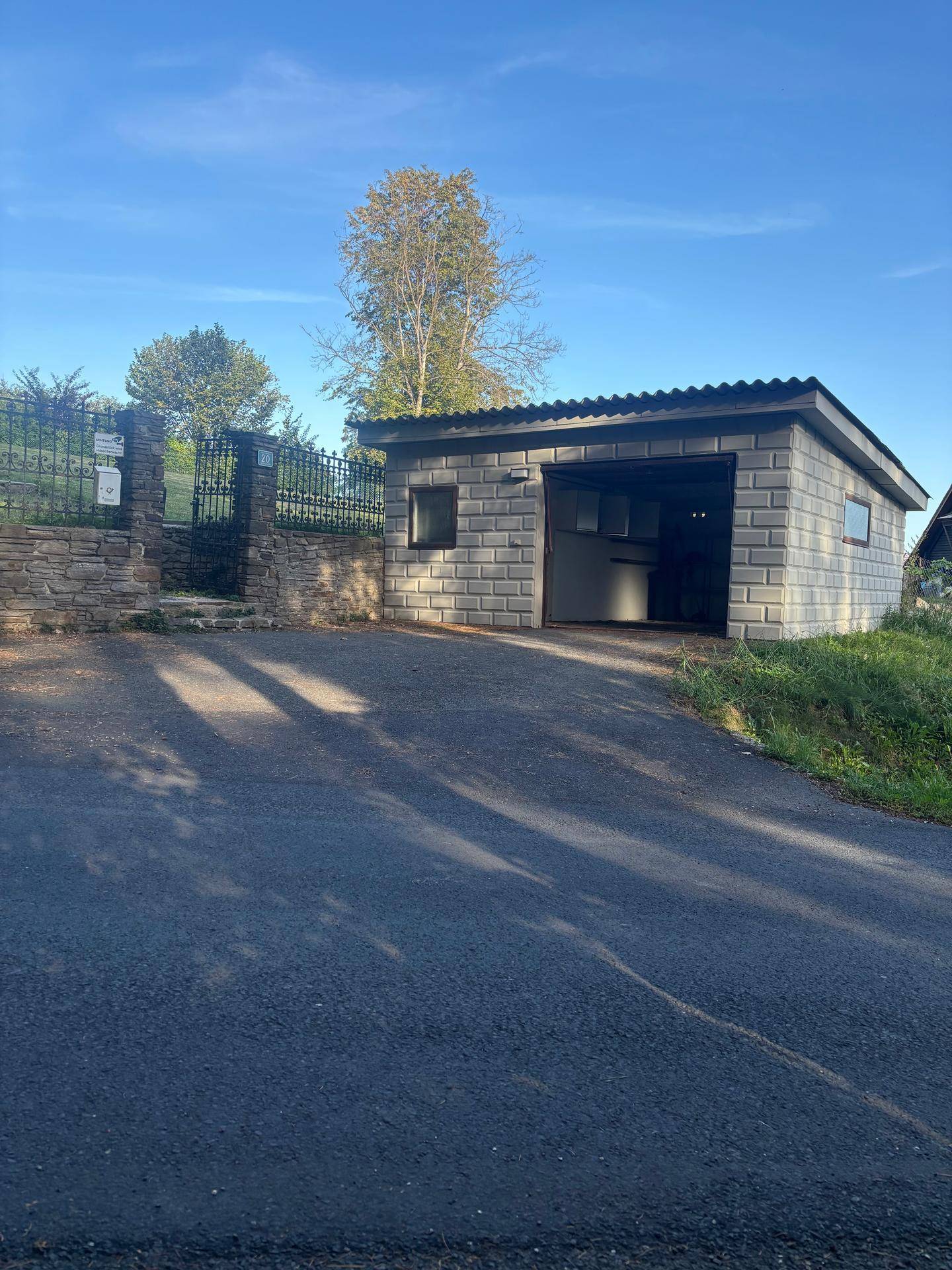 Freistehende Garage mit offenem Tor und Zufahrt, umgeben von einer Steinmauer und einem Zaun.