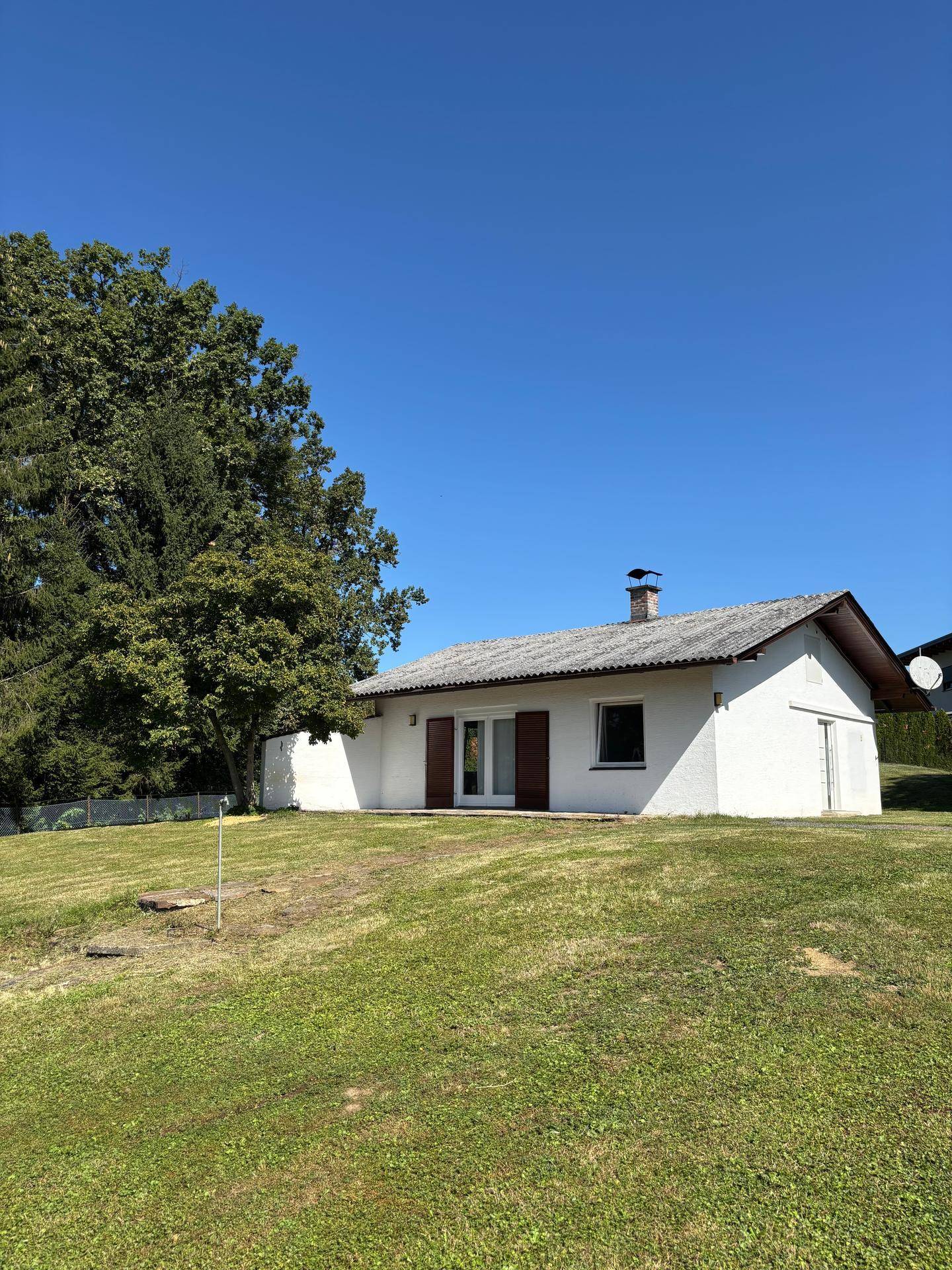 Rückansicht des Hauses mit Schornstein und weitläufiger Rasenfläche unter blauem Himmel.