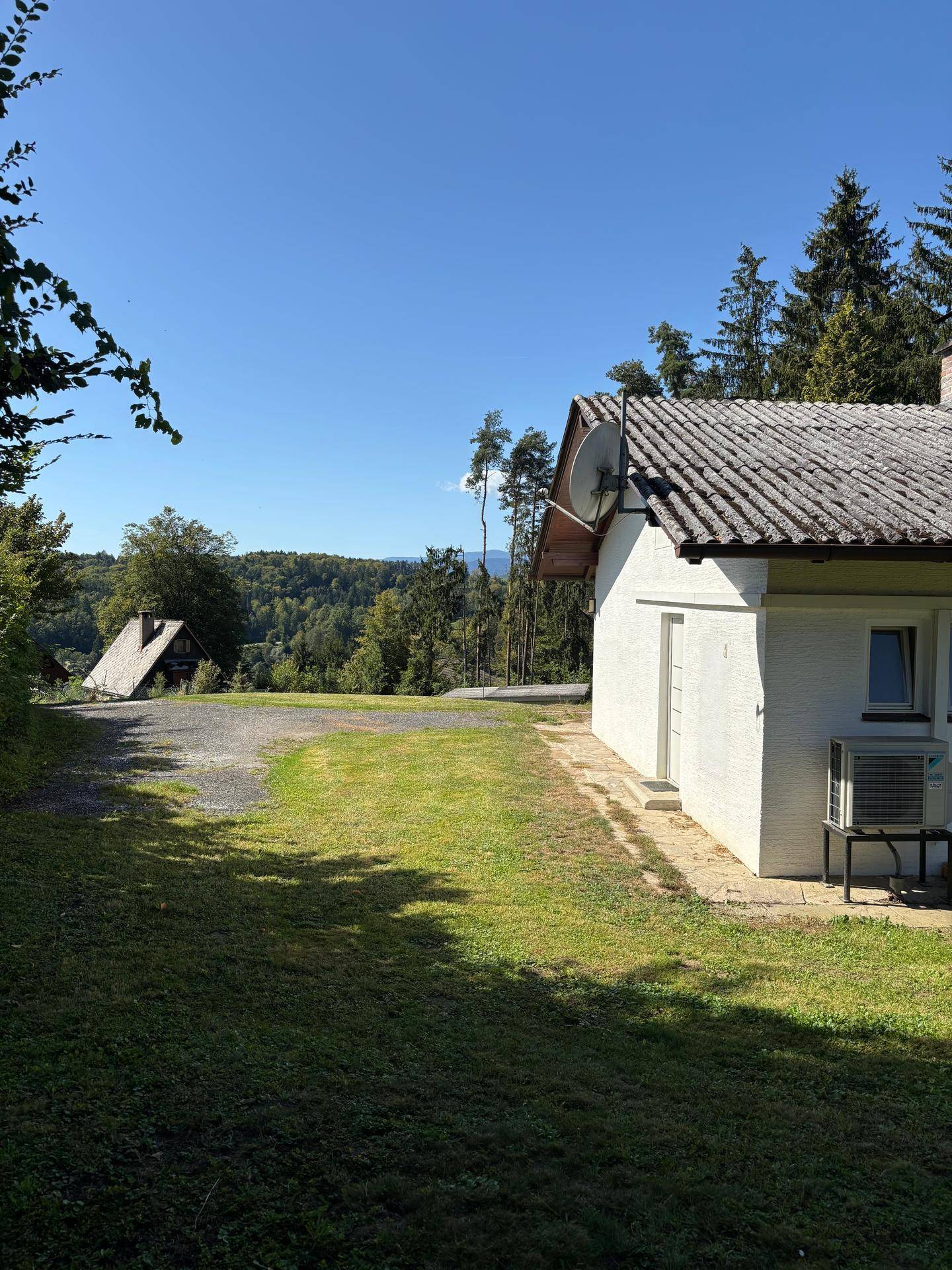 Seitenansicht des Hauses mit Blick auf eine bewaldete Hügellandschaft und blauen Himmel.
