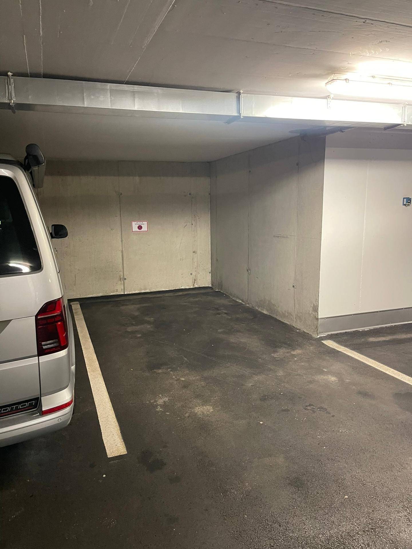Geräumiger Tiefgaragenstellplatz mit Betonwänden und heller Beleuchtung, neben einem geparkten Fahrzeug.