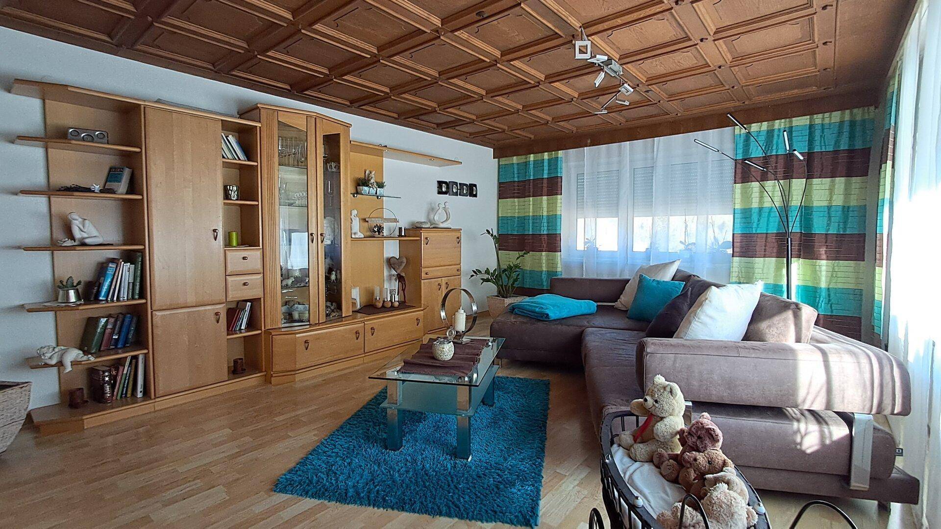 Helles Wohnzimmer mit Holzkassettendecke, Parkettboden, großer Wohnwand und bequemer Couch.