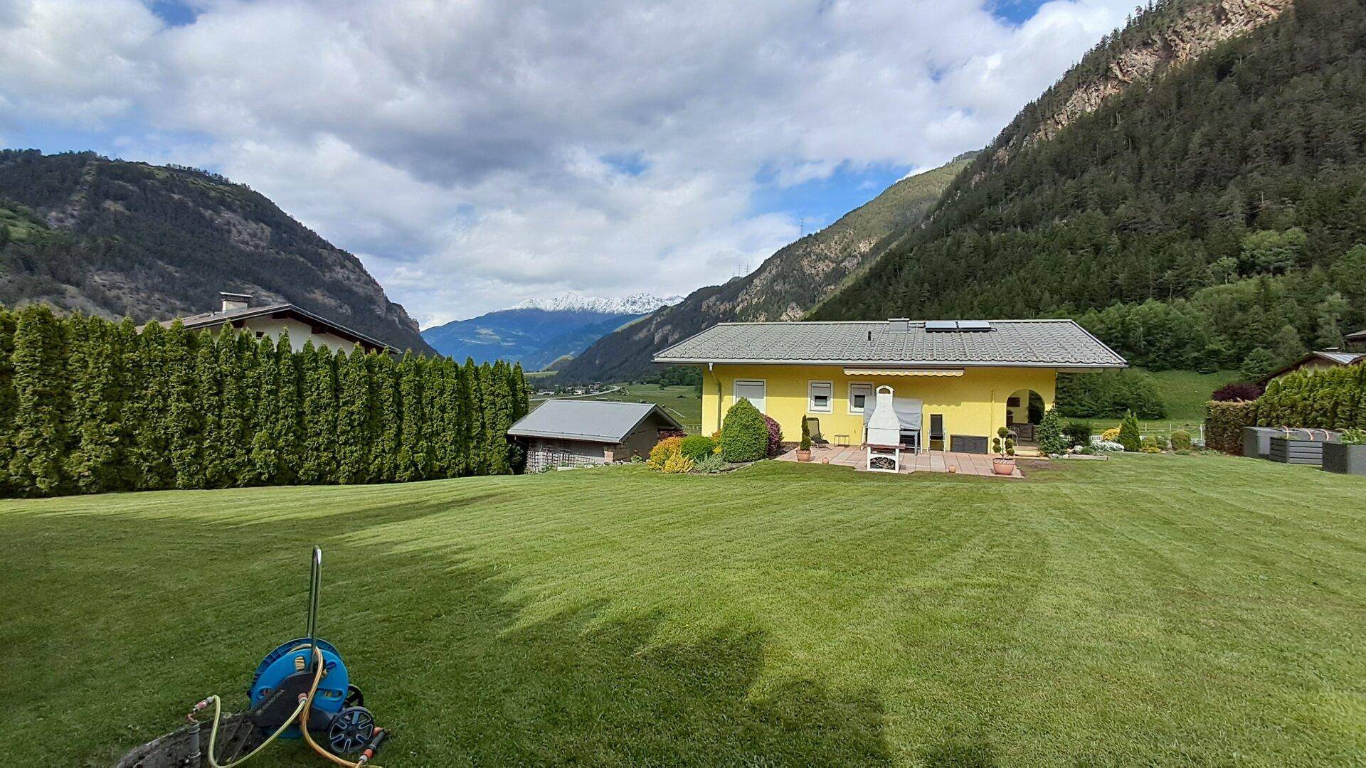 Großzügiger Garten mit einem Haus und weitem Blick auf das Tal und die umliegenden Berge.