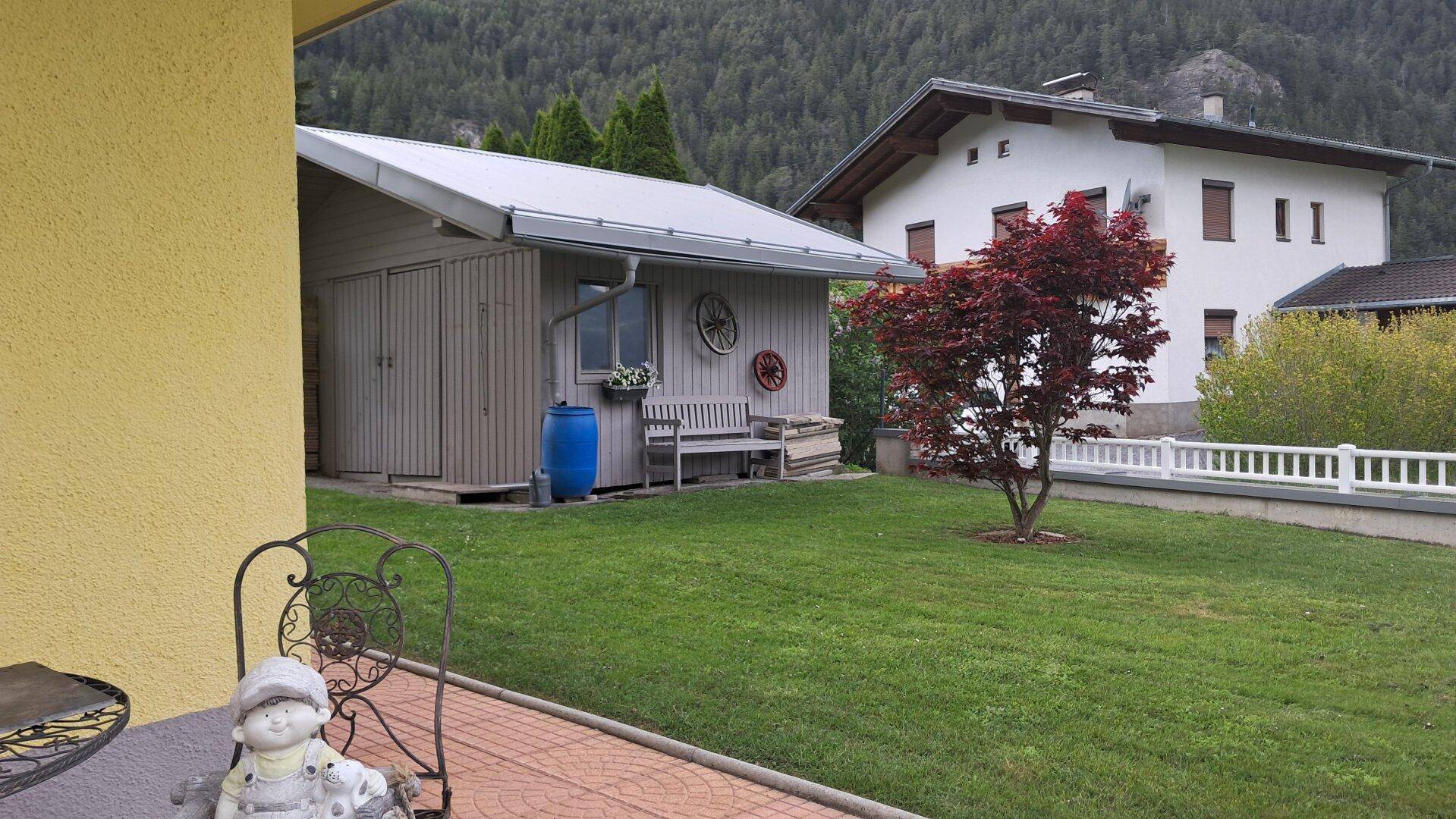 Kleiner Gartenbereich mit einem Holzschuppen und einer gepflasterten Fläche neben dem Haus.