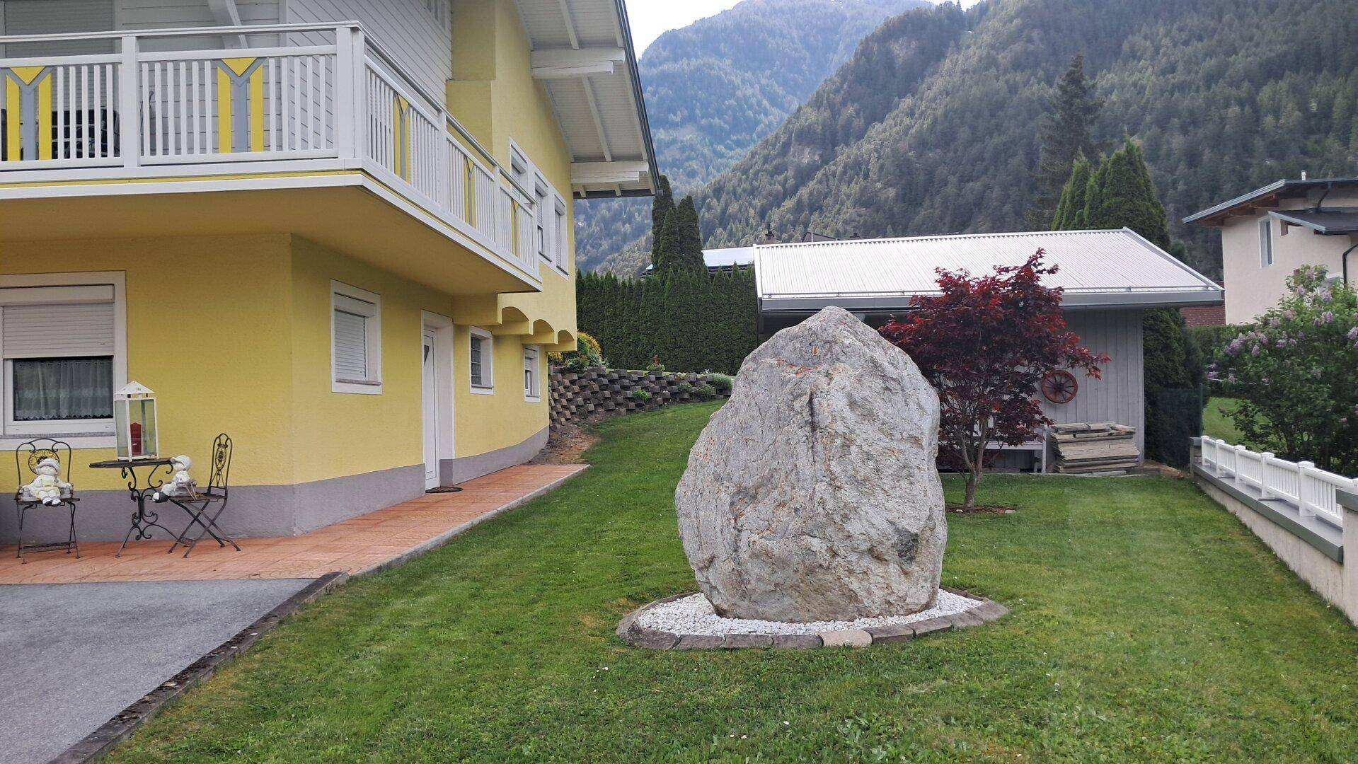 Dekorativer Felsen im gepflegten Gartenbereich mit Rasen und dem Haus im Hintergrund.