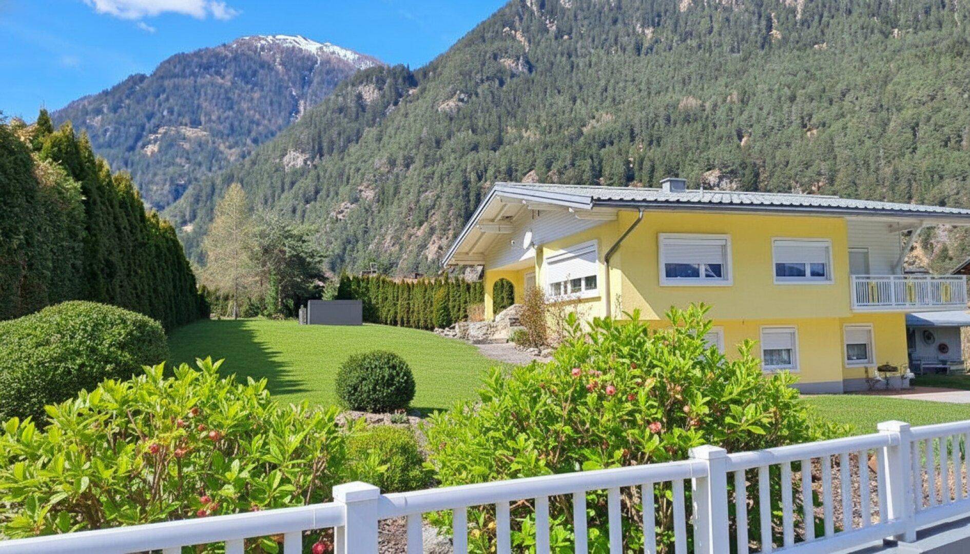 Gepflegter Gartenbereich mit einem charmanten Haus und einem weiten Blick auf die Berge.
