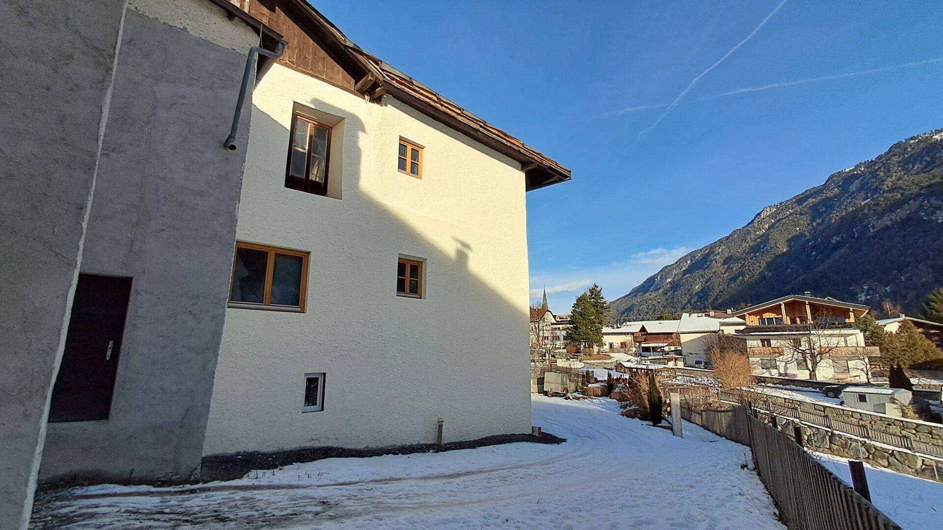 Seitenansicht eines Gebäudes in verschneiter Landschaft mit Blick auf die umliegenden Berge und Häuser.