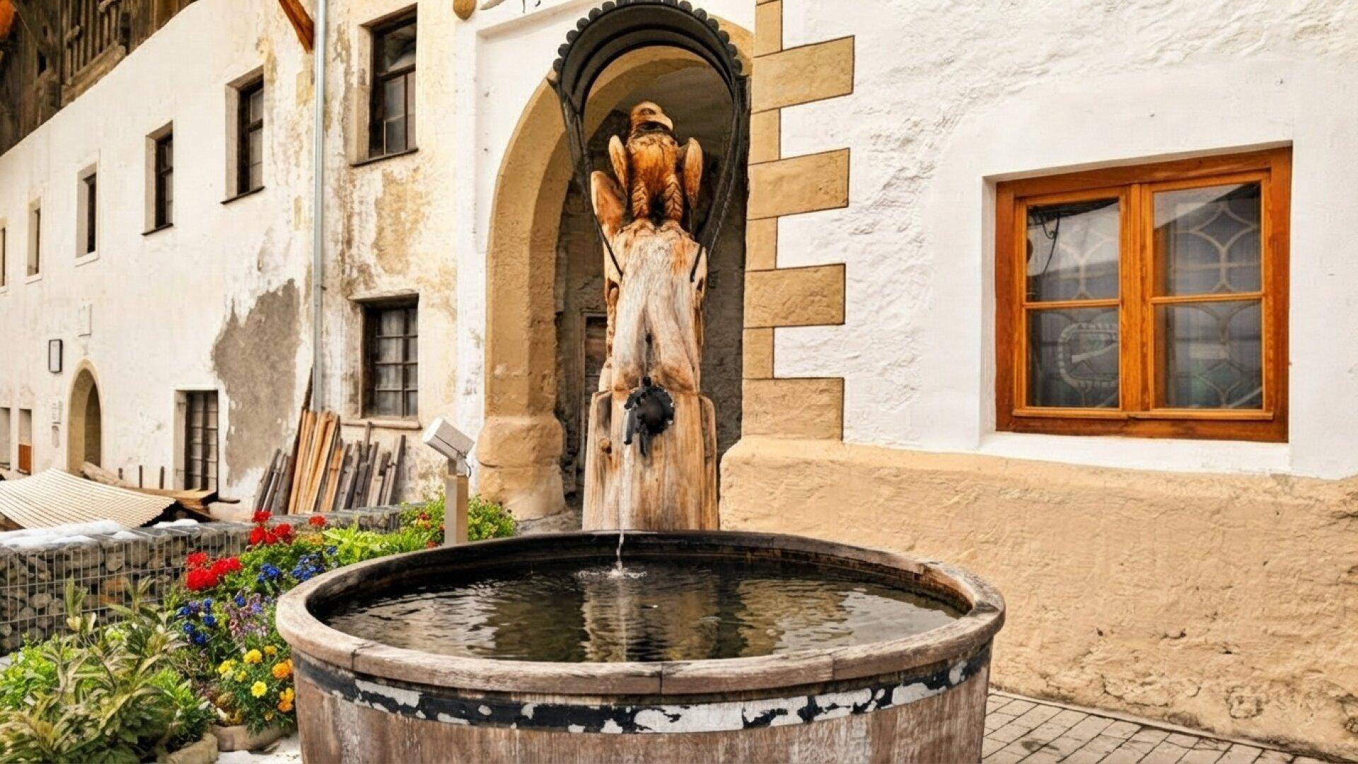 Traditioneller Innenhof mit einem hölzernen Brunnen und einer geschnitzten Figur, umgeben von historischen Gebäuden.