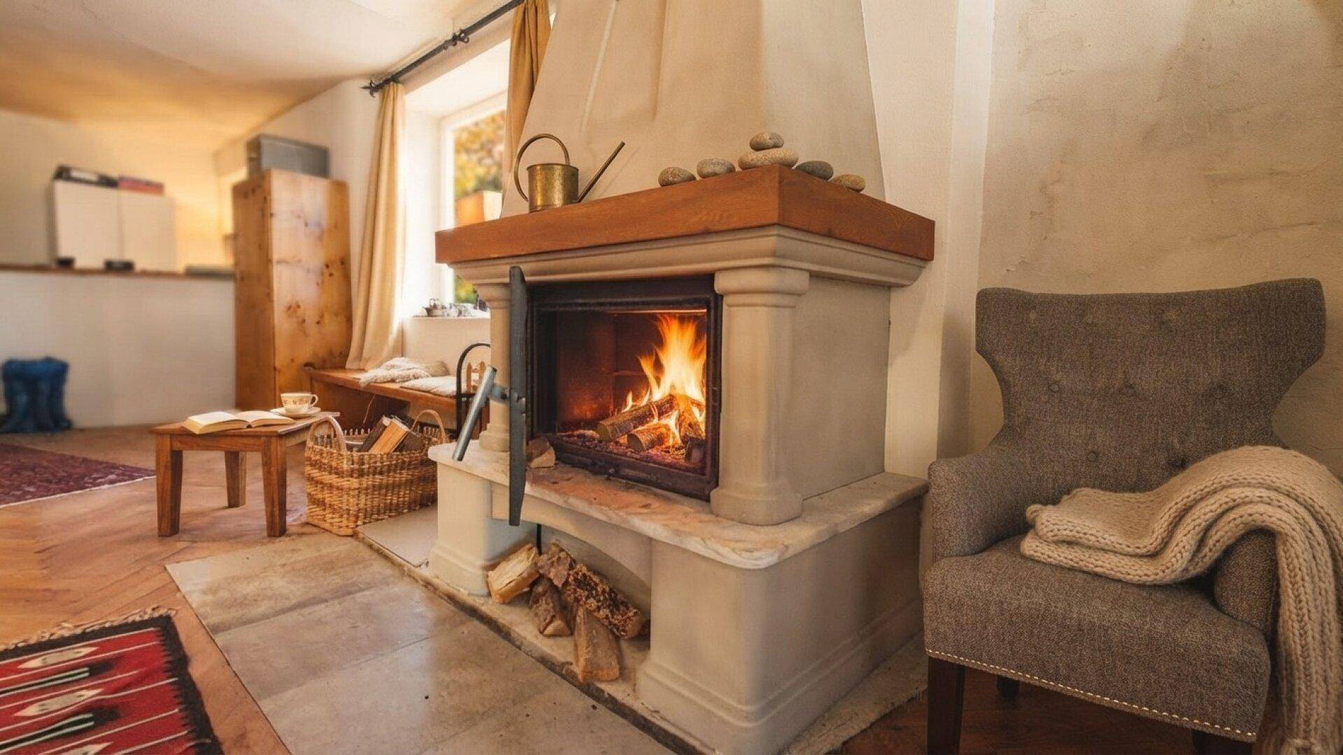 Gemütliches Wohnzimmer mit einem steinernen Kamin, bequemen Sessel und rustikalen Holzelementen.