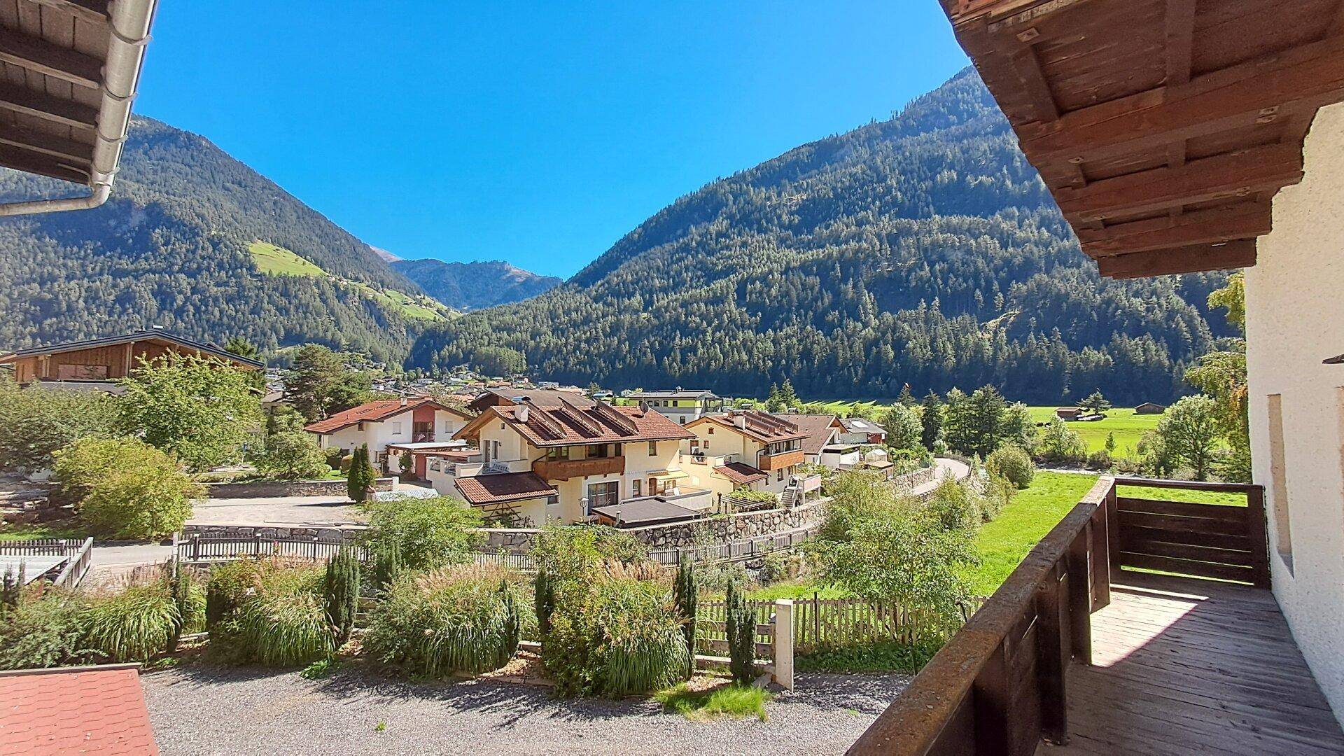 Blick vom Balkon auf ein malerisches Dorf, grüne Wiesen und die umliegende Berglandschaft.