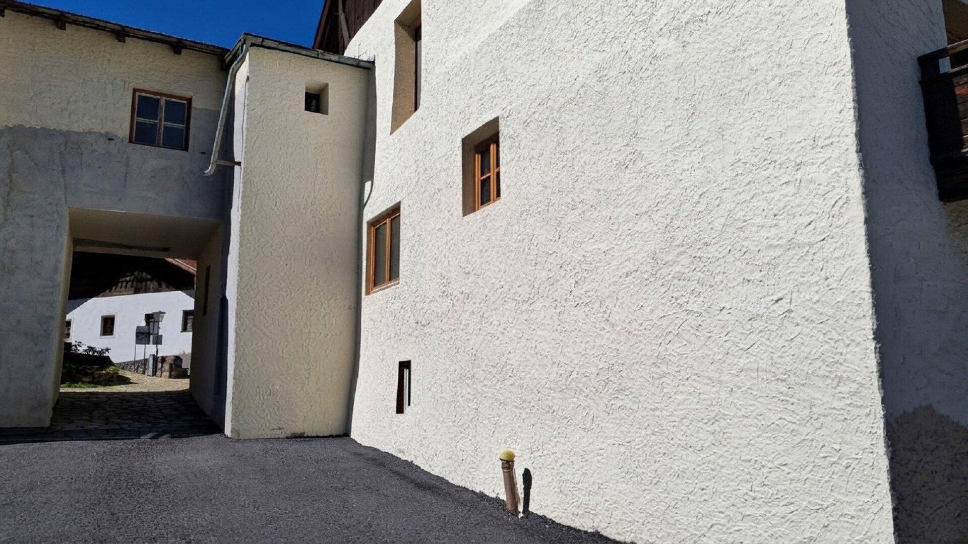 Fassade eines Gebäudes mit rauer Putzstruktur und einem Durchgang zu einem Innenhof in sonniger Umgebung.