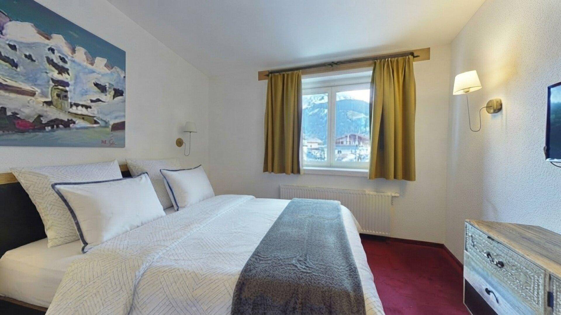 Schlafzimmer mit Doppelbett, rotem Teppichboden und einem Fenster mit malerischem Bergblick.