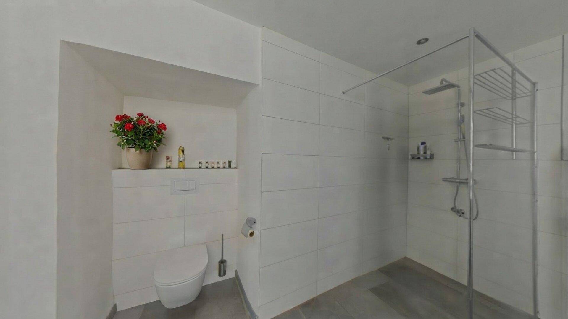 Modernes Badezimmer mit wandhängender Toilette und einer geräumigen, ebenerdigen Dusche.