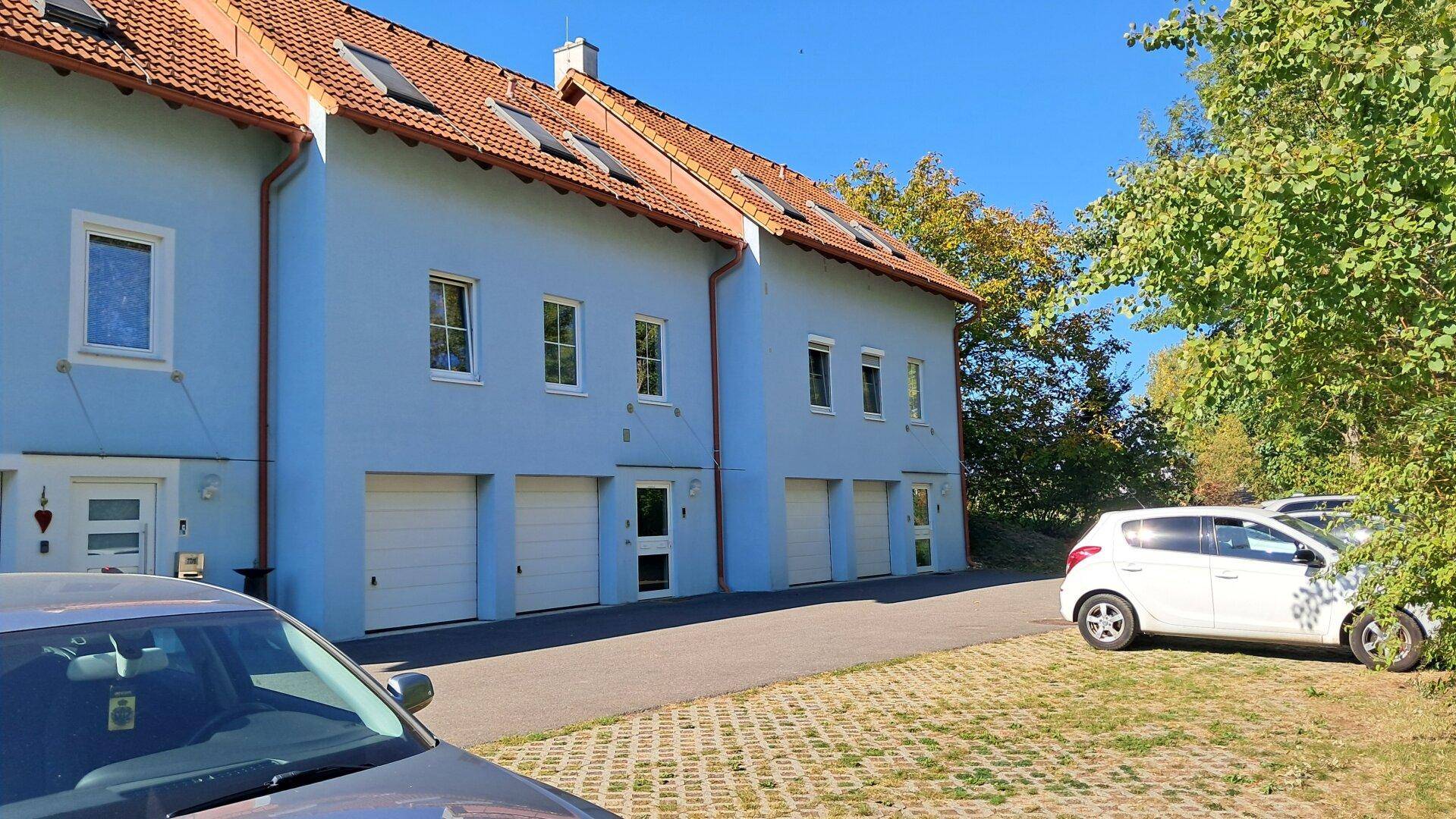 Reihe von blauen Reihenhäusern mit Garagen und Parkplätzen im Freien.