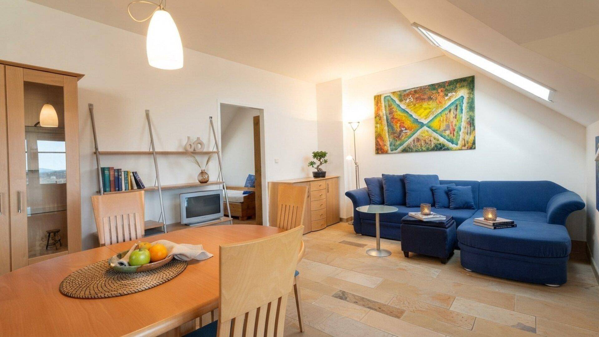 Heller Wohn-Essbereich im Dachgeschoss mit blauer Couch und Holztisch.