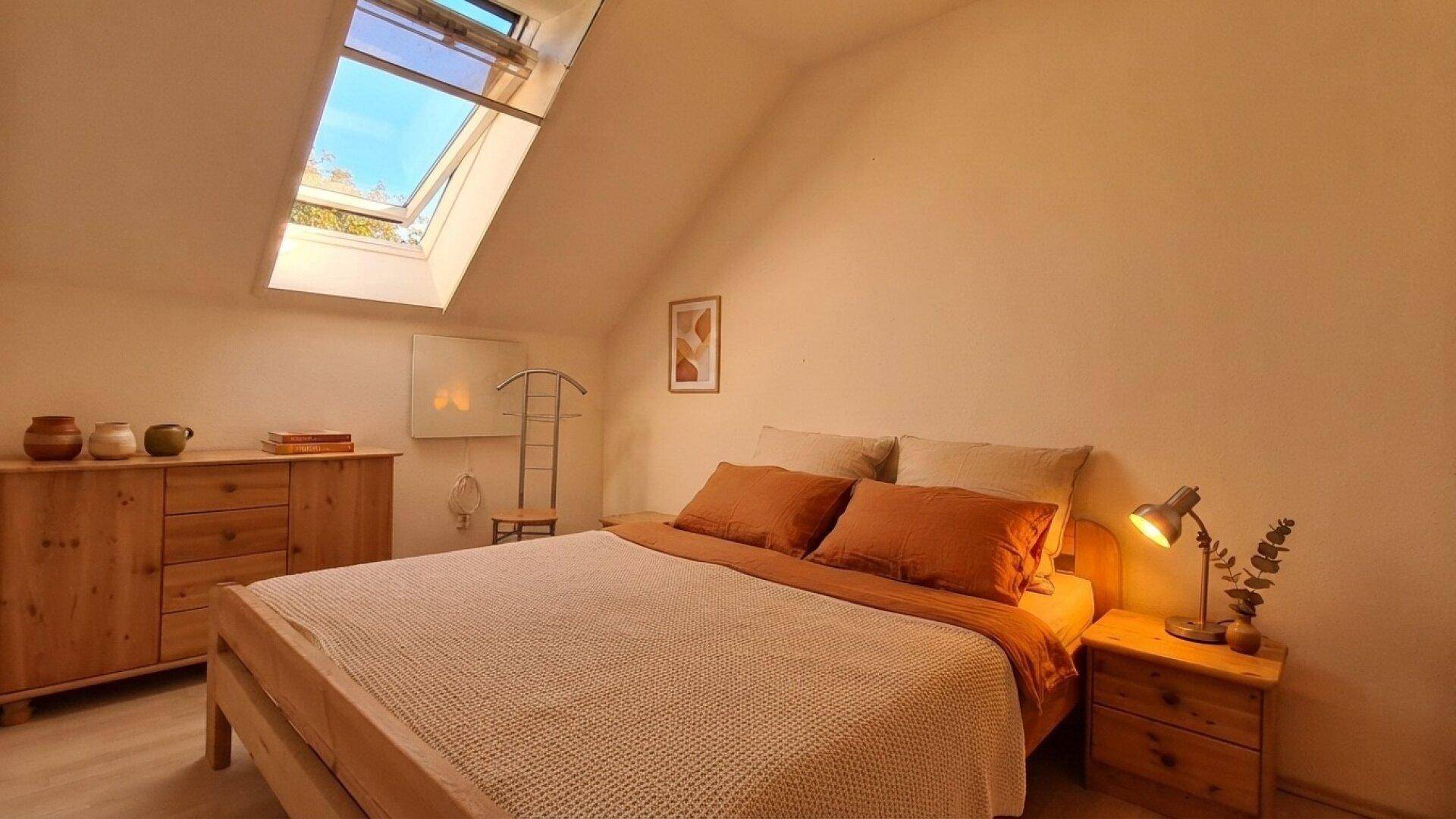 Helles Schlafzimmer im Dachgeschoss mit Holzbett, Kommode und Dachfenster.