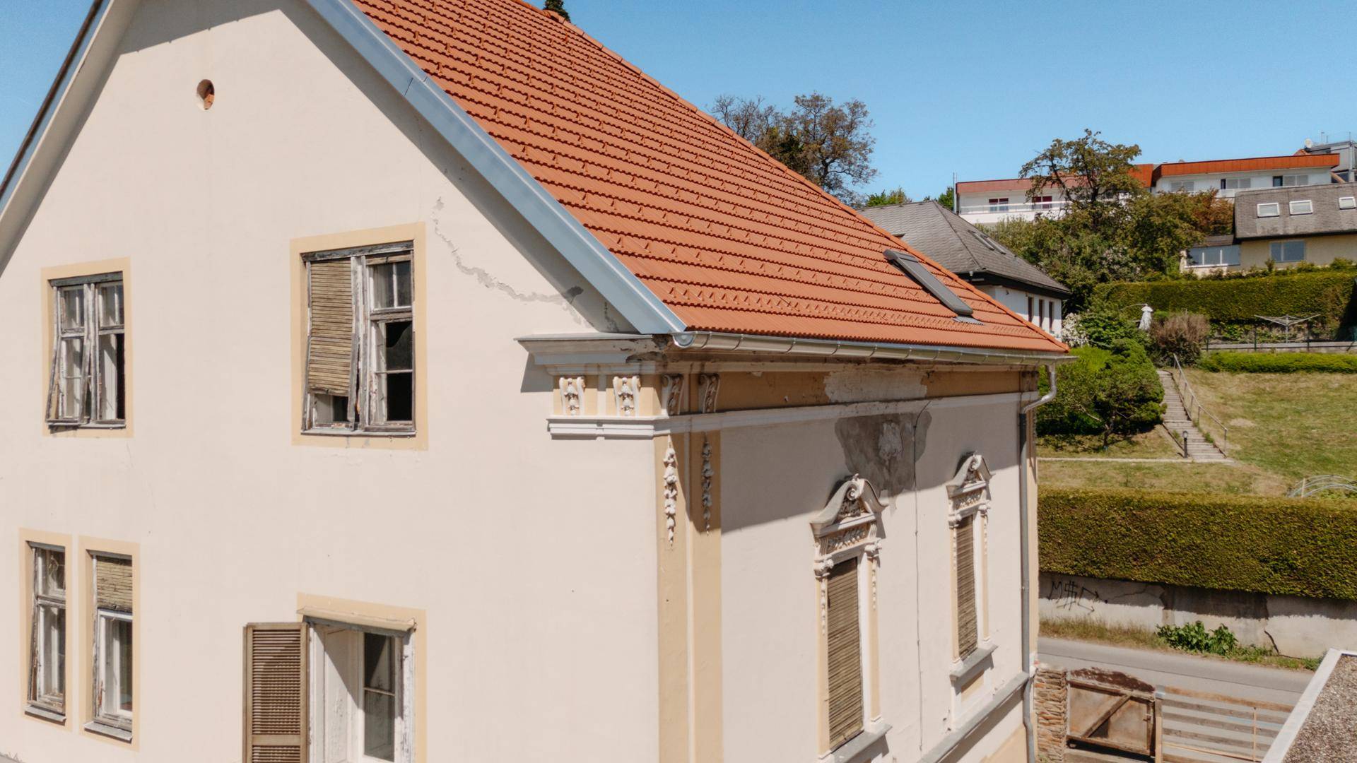 Seitenansicht des historischen Gebäudes mit Ziegeldach, Fensterläden und verwitterter Fassade.