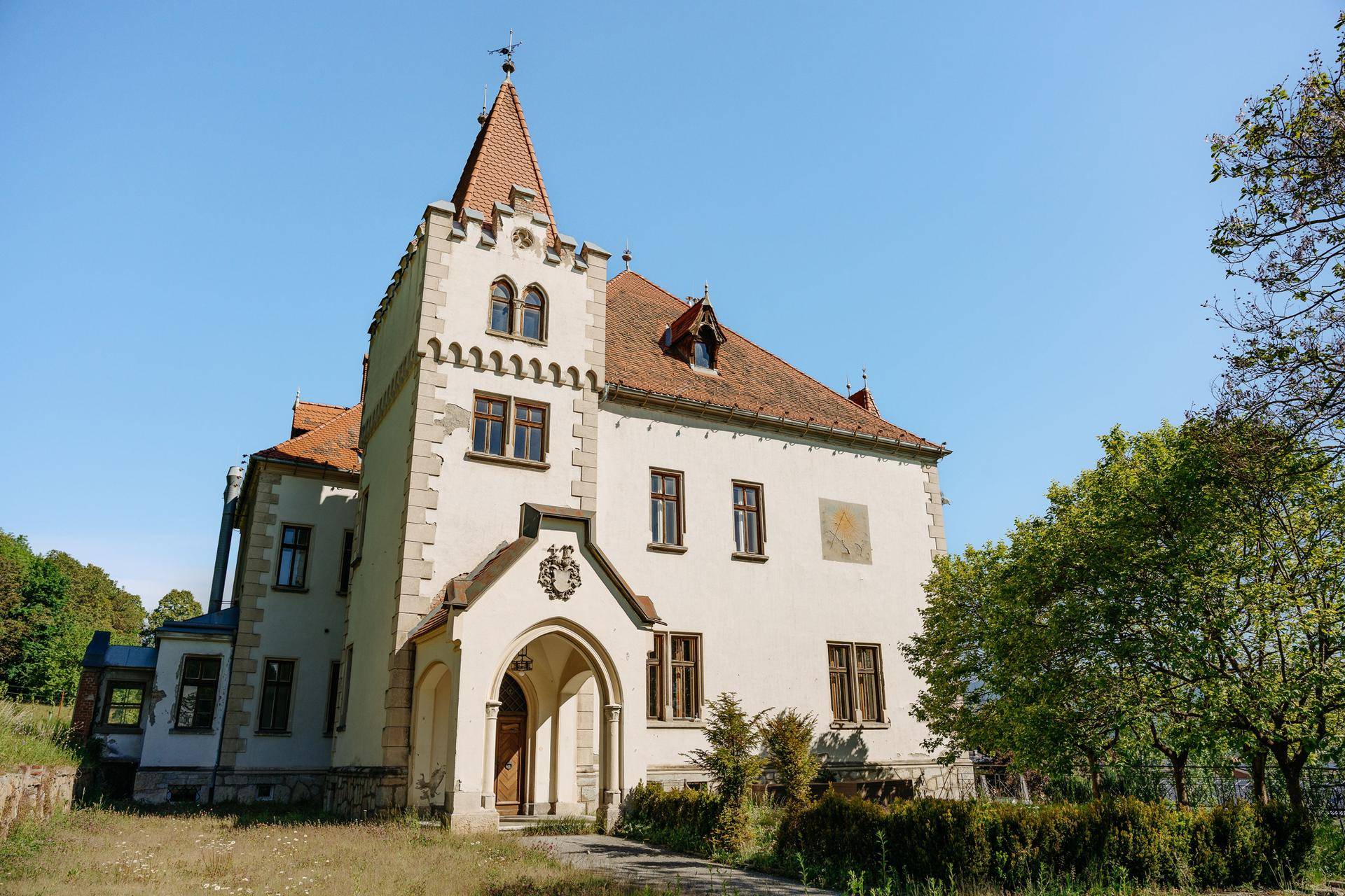 Historisches Gebäude mit markantem Turm, weißer Fassade und rotem Ziegeldach.