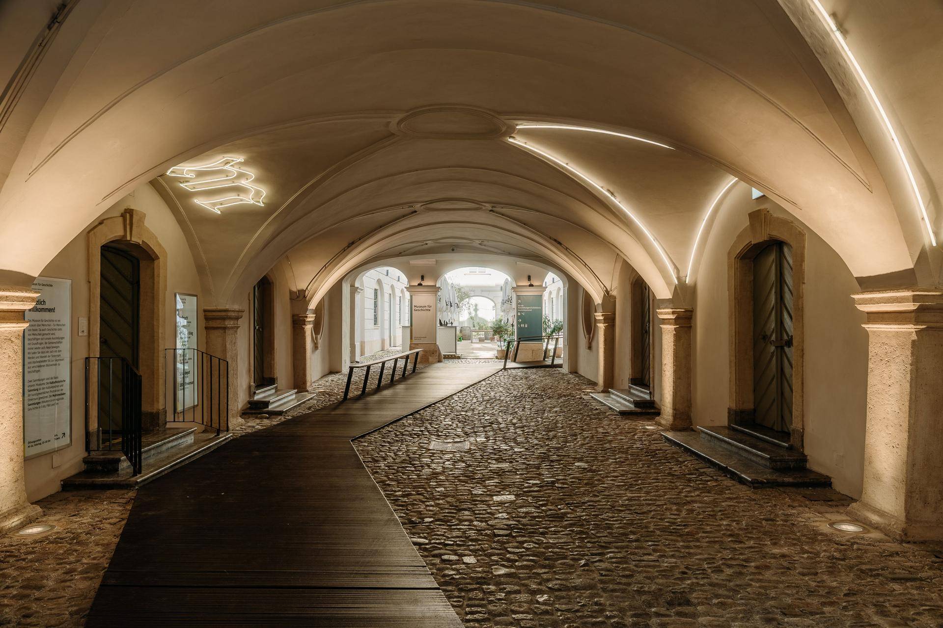 Historischer, gewölbter Durchgang mit Kopfsteinpflaster und moderner Beleuchtung in einem alten Gebäude.