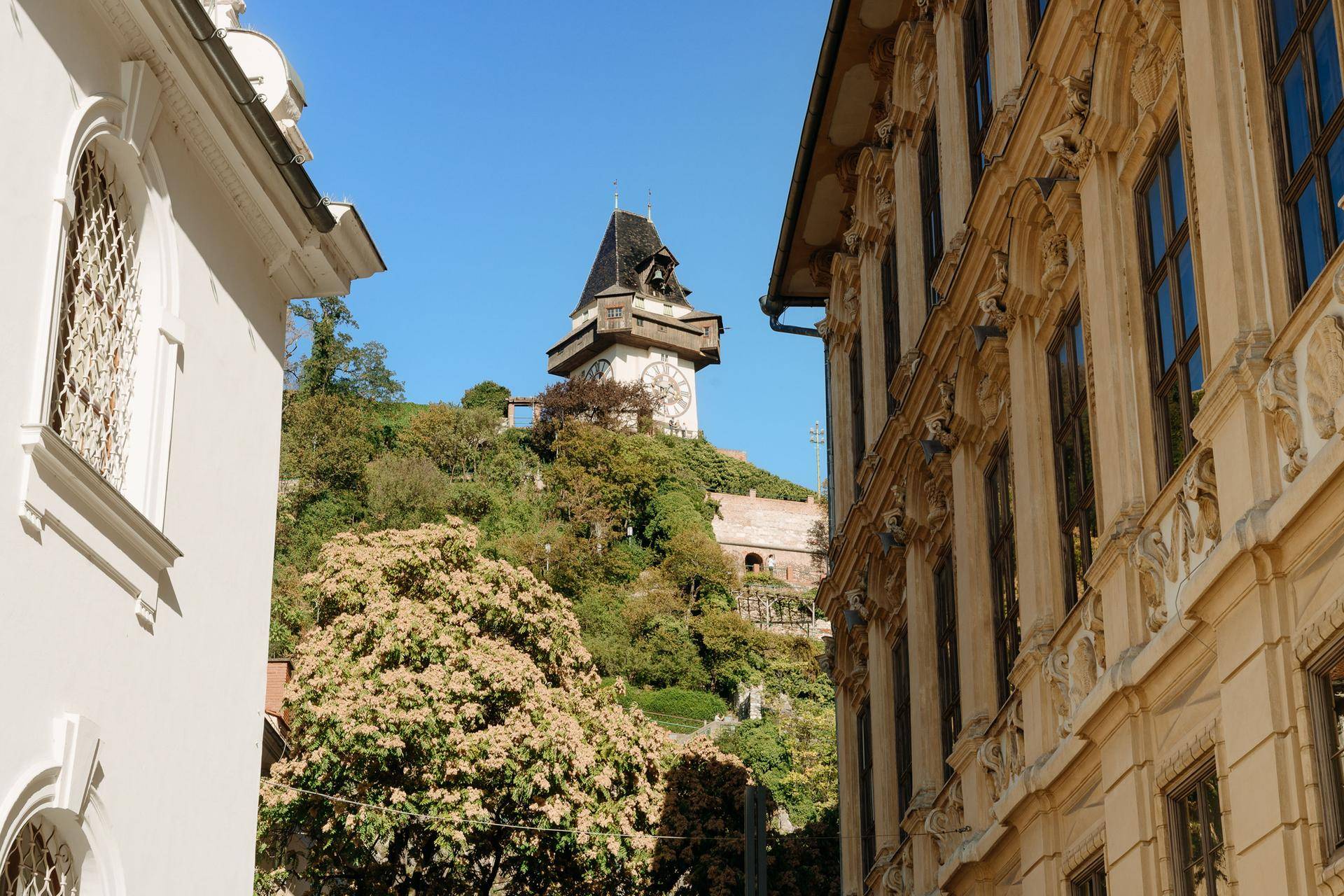 Historisches Gebäude mit Blick auf den Uhrturm am Schlossberg in Graz unter blauem Himmel.