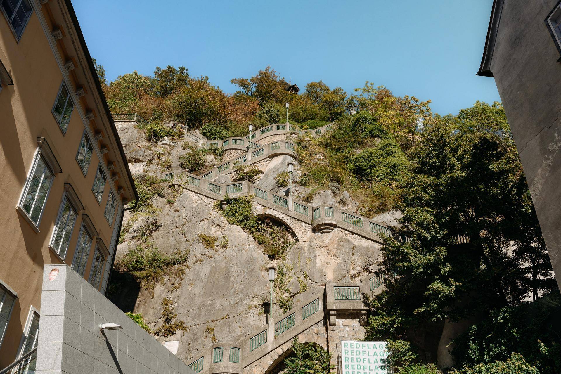 Historische Steintreppe mit grünen Geländern, die sich einen felsigen Hügel hinaufschlängelt.
