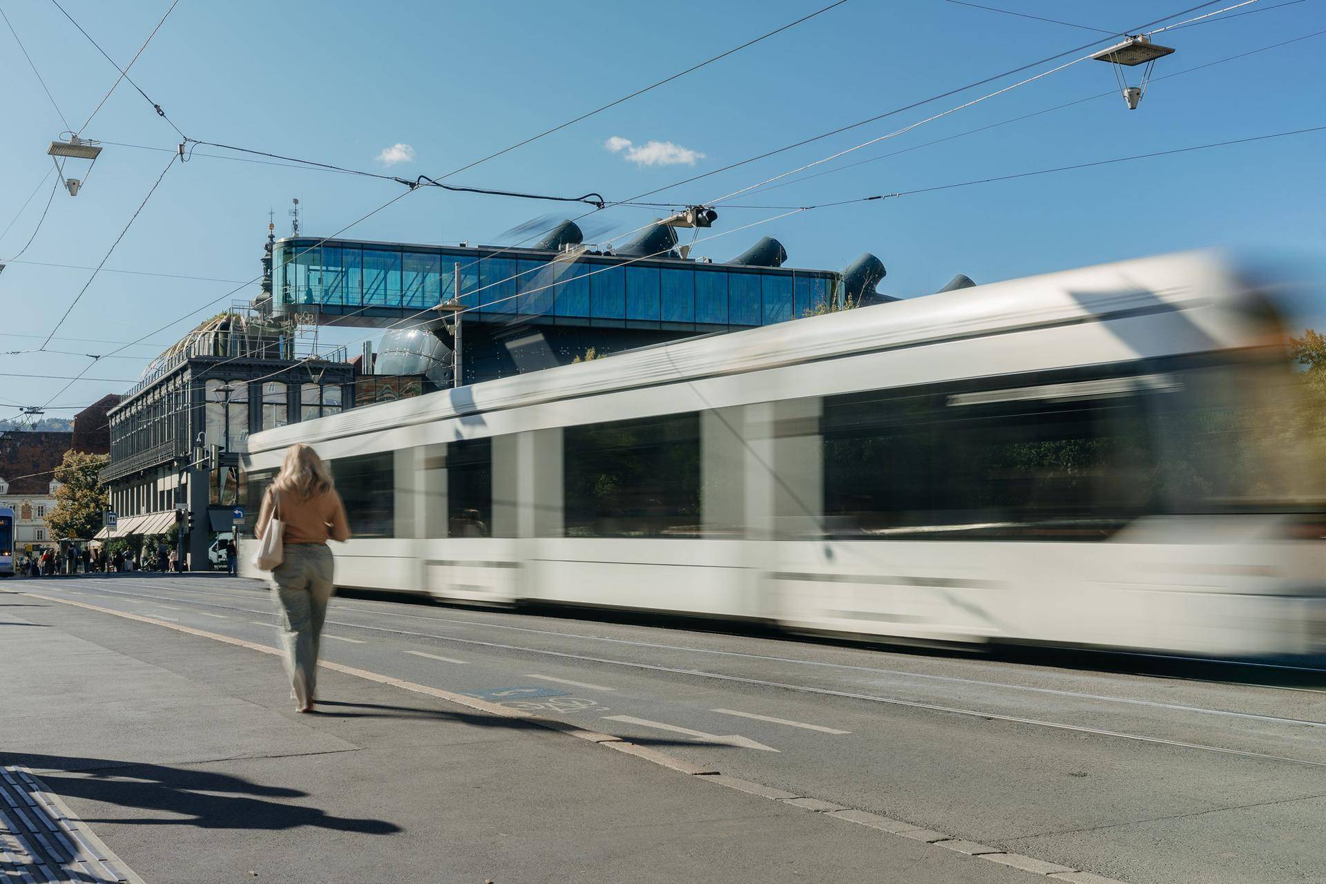 Straßenszene mit einer vorbeifahrenden Straßenbahn vor einem modernen Gebäude.
