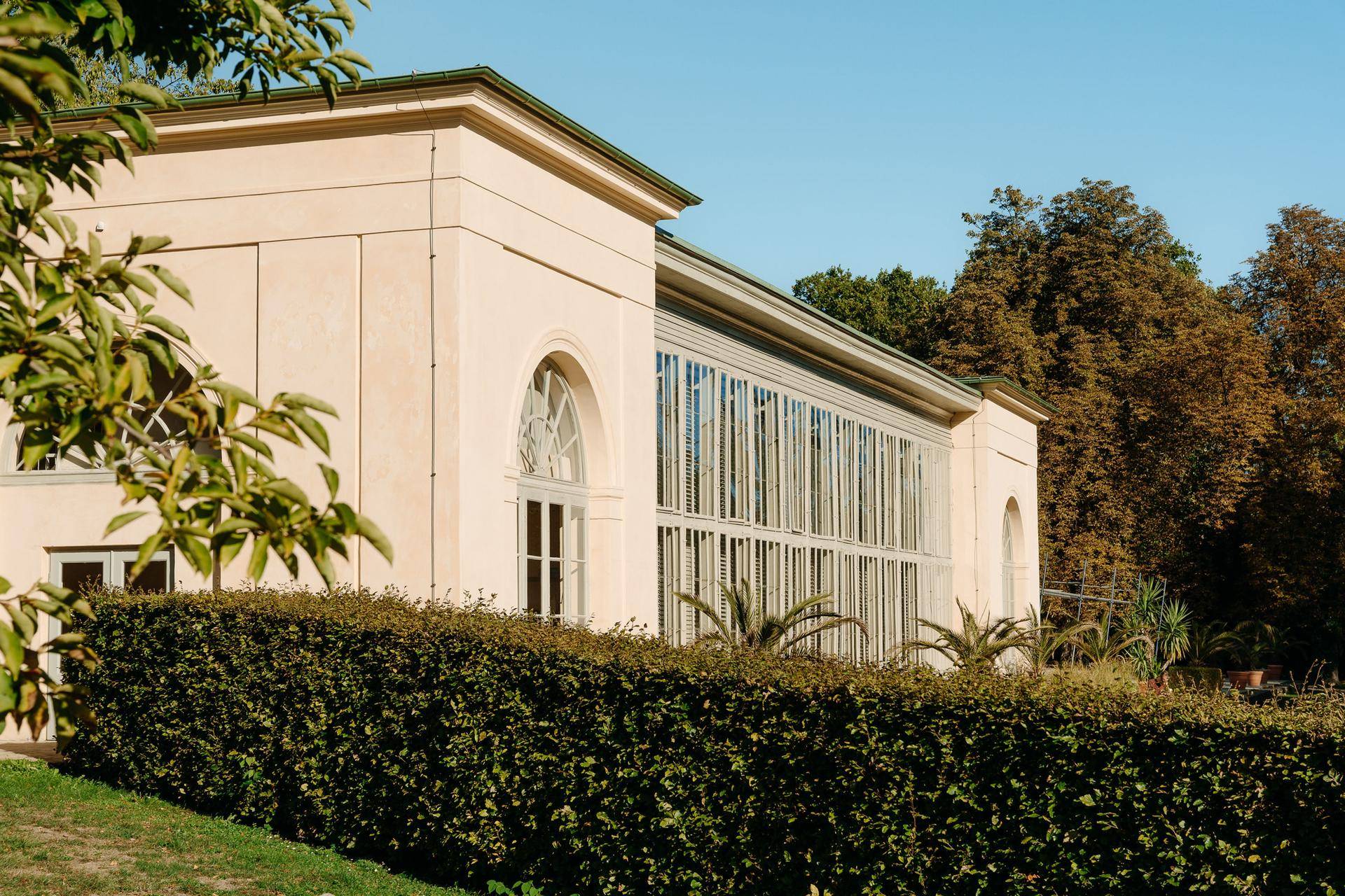 Klassisches Gebäude mit großen Fenstern und einer gepflegten Hecke im Vordergrund.