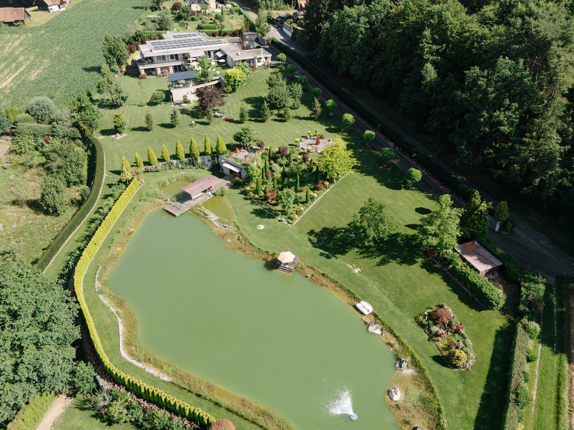 Weitläufiges Anwesen mit großem Teich, umgeben von grünen Feldern und Wäldern unter blauem Himmel.