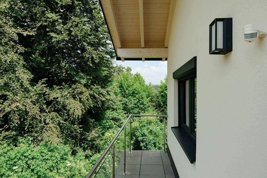 Kleiner Balkon mit Glasgeländer und weitem Blick in die umliegende Waldlandschaft.