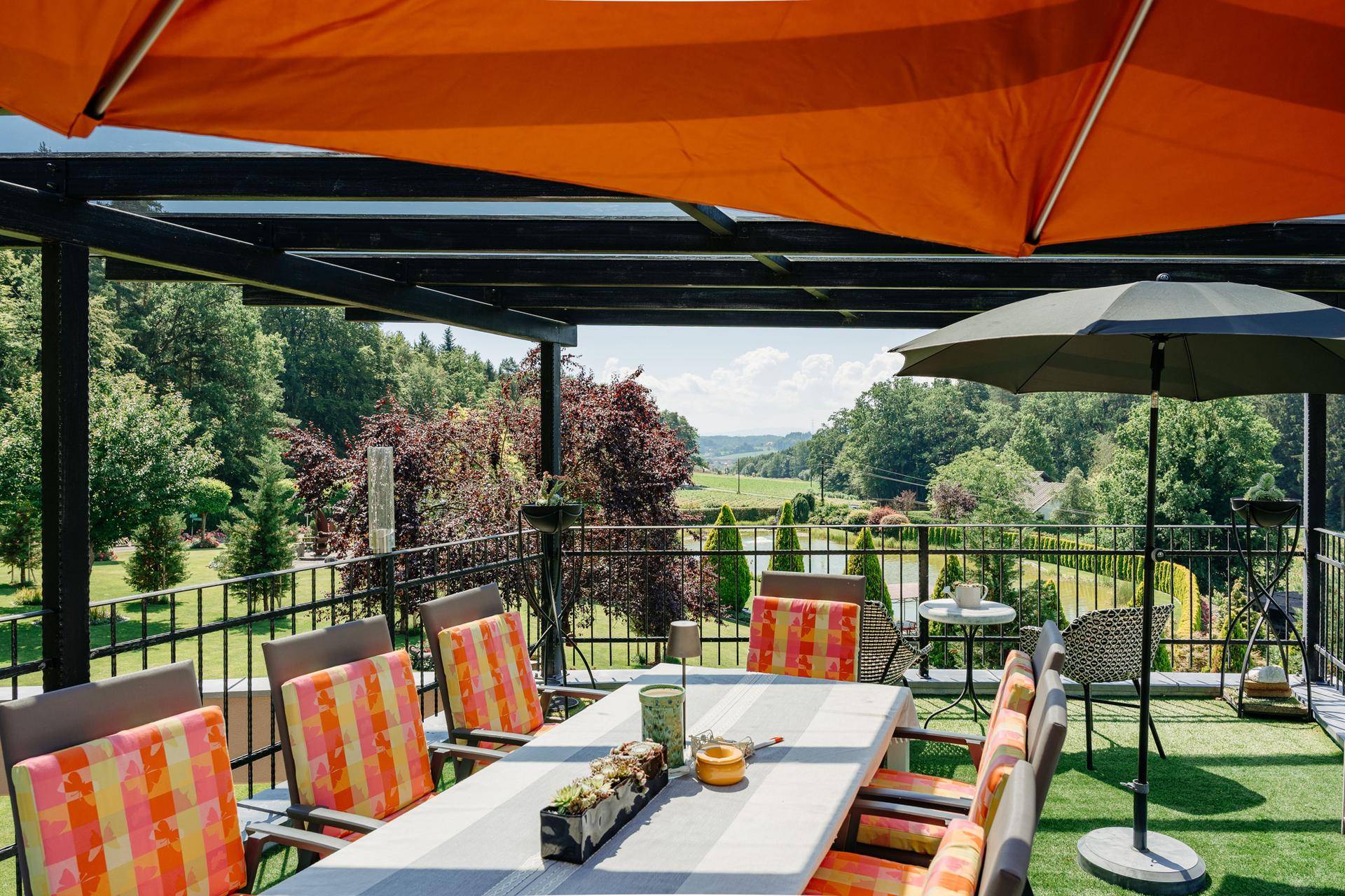 Überdachte Terrasse mit Esstisch und Stühlen, die einen weiten Blick über die grüne Landschaft bietet.