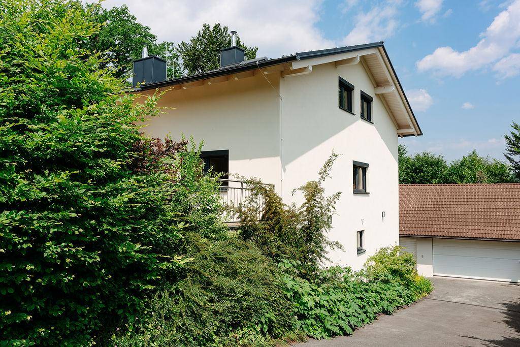 Seitenansicht des Hauses umgeben von üppigem Grün mit separater Garage im Hintergrund.