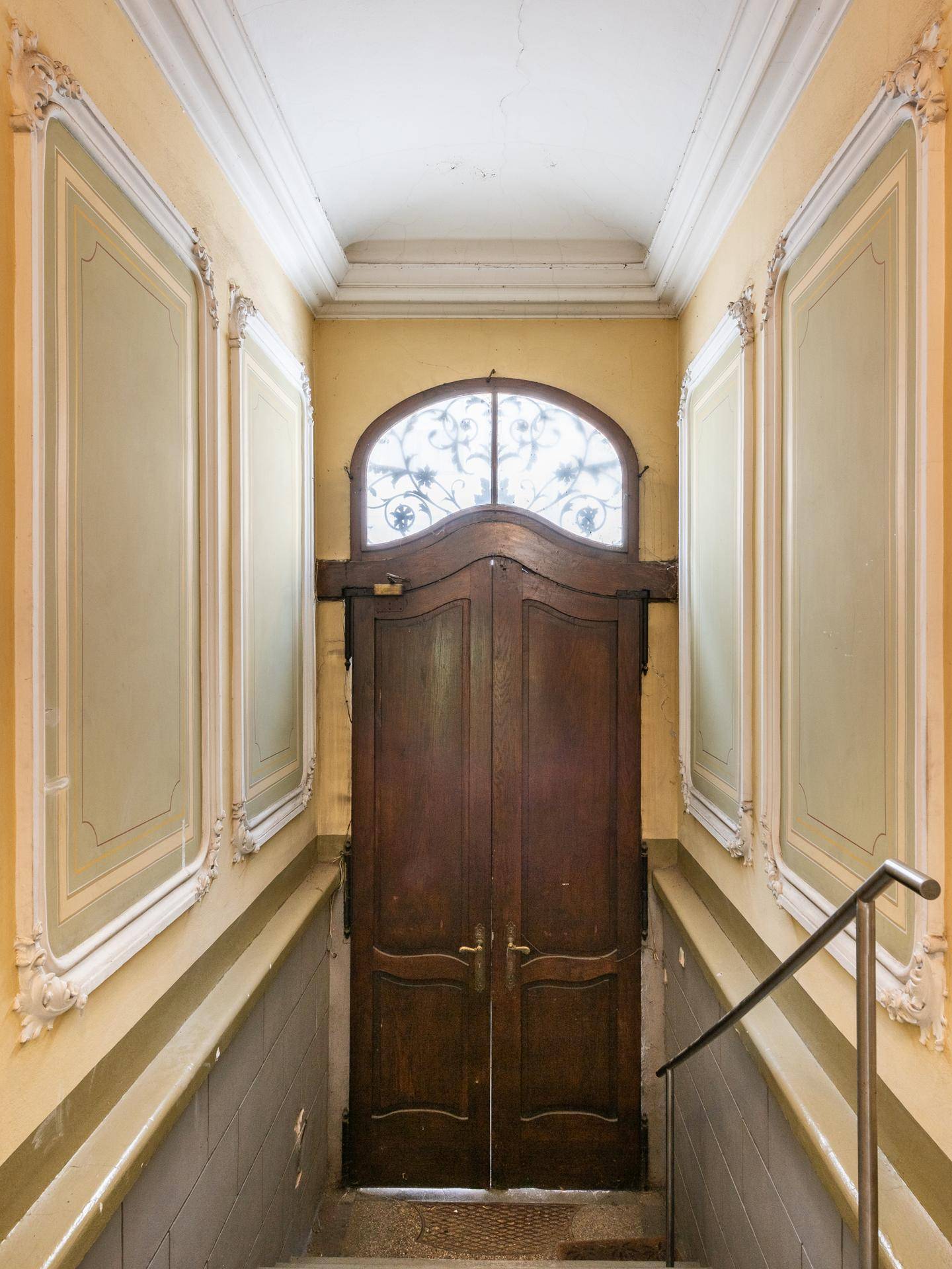 Historischer Eingangsbereich mit Holztür, Bogenfenster und Treppenaufgang.