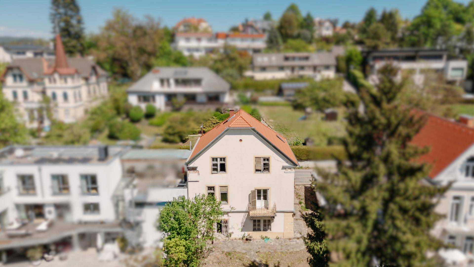 Luftaufnahme eines charmanten Hauses mit rotem Dach in einer grünen Wohngegend mit weiteren Gebäuden.