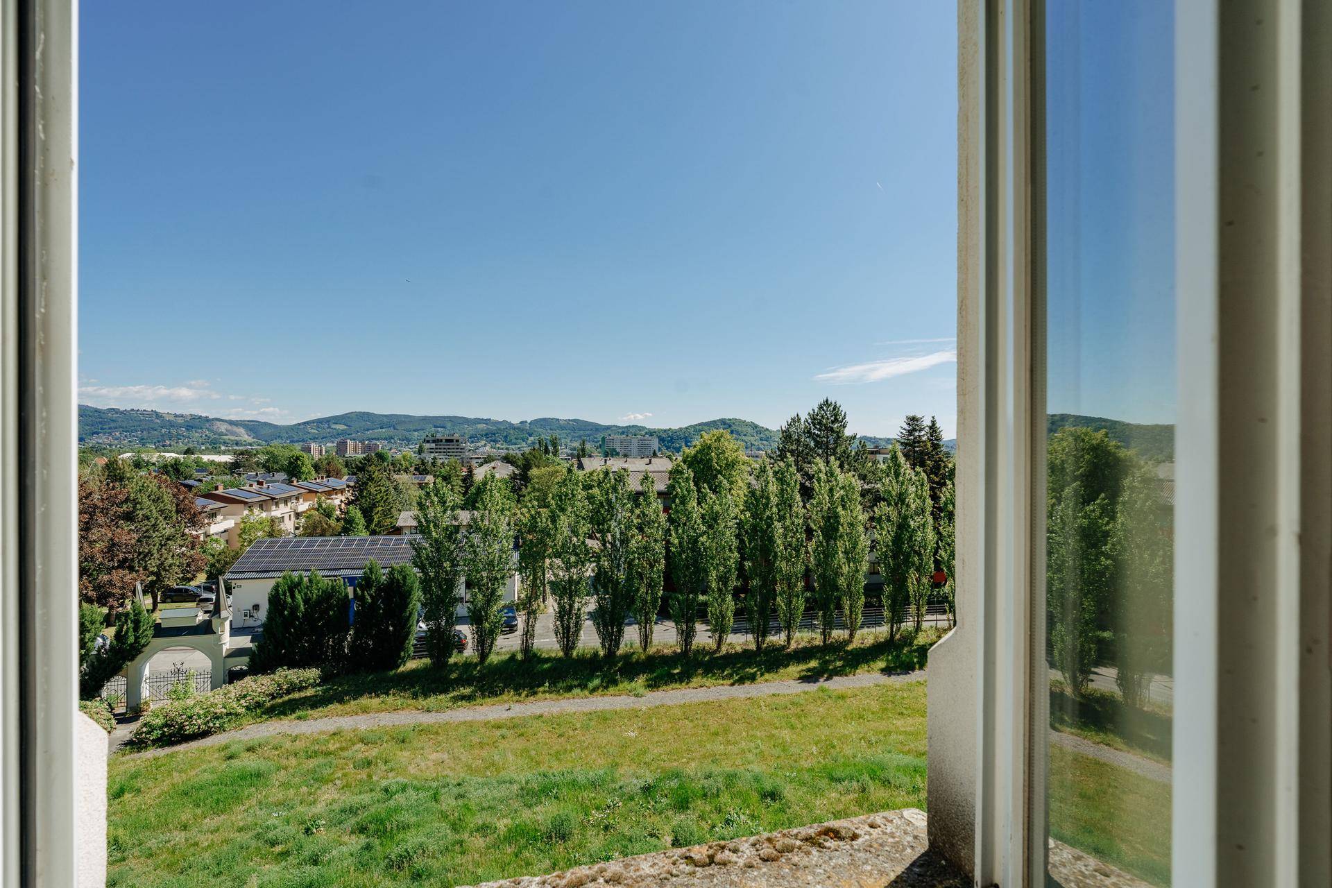Weitblick aus dem Fenster über eine grüne Landschaft und die umliegende Stadt.