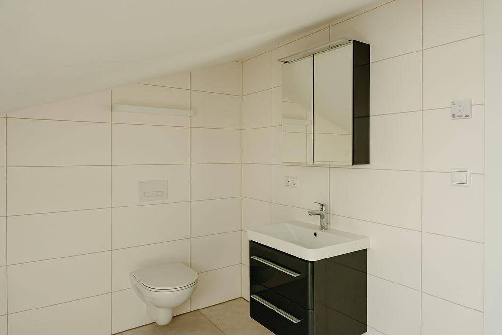 Modernes Badezimmer mit Waschtisch, Spiegelschrank und Wand-WC, hell gefliest.