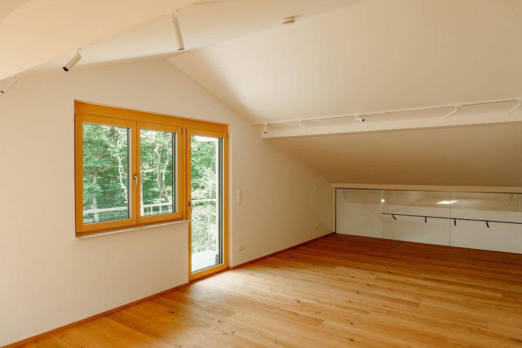 Helles Zimmer mit Holzboden, Dachschräge und Fenster mit Blick ins Grüne.